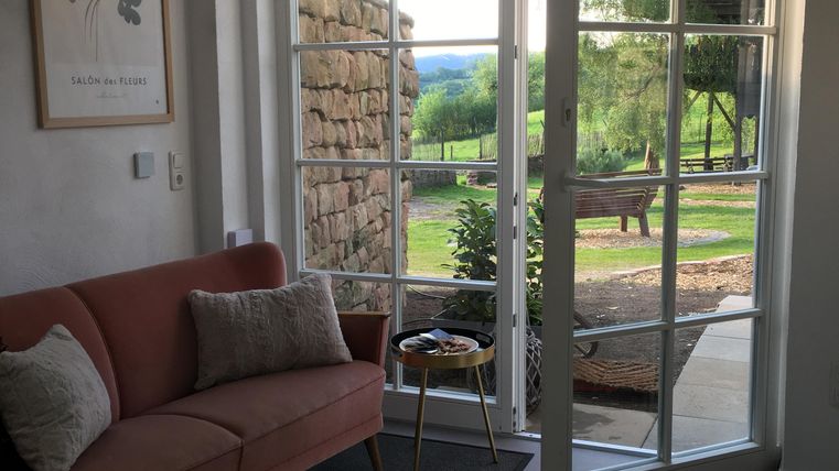 Un salon confortable avec un canapé rose et une table. Les grandes fenêtres offrent une belle vue sur le jardin et le paysage extérieur.
