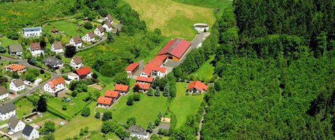 Eine idyllische Landschaft mit mehreren Häusern und einem großen Bauernhof. Der Hintergrund ist von Bäumen und Feldflächen umgeben.