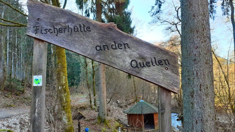 Panneau en bois avec l'inscription 'Cabane de pêcheur aux sources' dans la forêt.