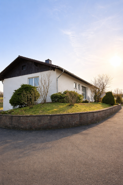 Ein modernes Einfamilienhaus mit einem gepflegten Garten und einem asphaltierten Weg. Der Himmel ist klar und die Sonne scheint.