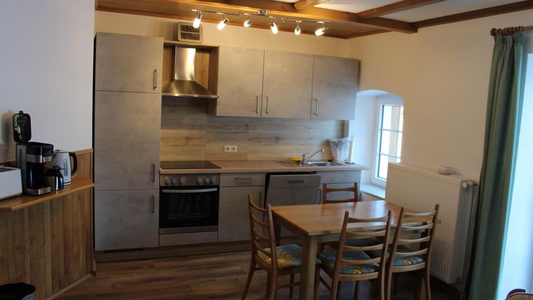 Eine moderne Küche mit einer Holzverkleidung und einem Esstisch. Der Raum ist hell und einladend mit großen Fenstern.