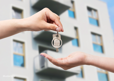 Eine Hand reicht einen Schlüssel mit einem Haus-Anhänger an eine andere Hand weiter.