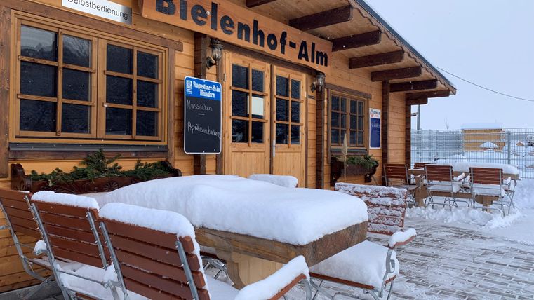 Eine verschneite Berghütte mit Holztischen und -stühlen im Freien.