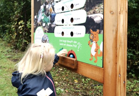 Een kind staat bij het leerstation &ldquo;Geen afval in het bos!&rdquo; op het natuurbelevingspad Gerolstein en haalt zijn bal uit het station.