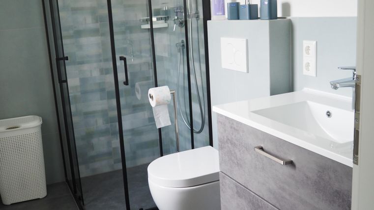 Ein modernes Badezimmer mit einer Dusche und einer eleganten Toilette. Die Wandverkleidung ist in sanften Farben gehalten, und es gibt einen großen Spiegel über dem Waschbecken.