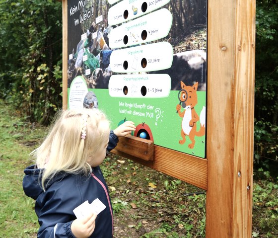 Ein Kind steht an der Lernstation "Kein M&uuml;ll im Wald!" auf dem Naturerlebnispfad Gerolstein und nimmt seine Kugel aus der Station.v