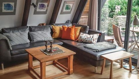 Ein gemütliches Wohnzimmer mit einem großen Sofa und bunten Kissen. Ein Holztisch und eine verfügbare Terrasse sind im Hintergrund sichtbar.