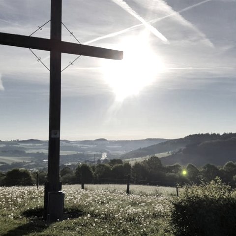 Holzkreuz auf einer Wiese, im Hintergrund die hügelige Landschaft der Eifel bei Sonnenaufgang., © Touristik GmbH Gerolsteiner Land