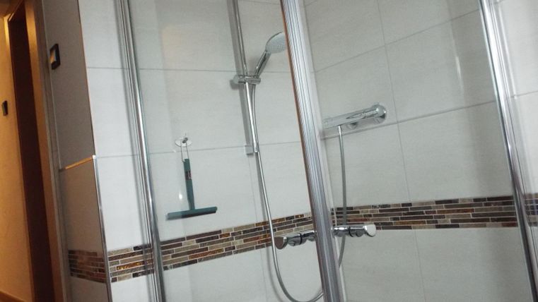 Eine moderne Dusche mit Glaswänden und einer Wandverkleidung aus Fliesen. Der Raum ist hell und sauber, mit einer klaren Struktur.