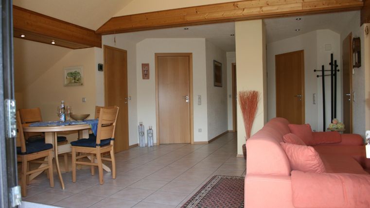 Ein helles und freundliches Wohnzimmer mit einer roten Couch und einem Esstisch. Der Raum hat Holzakzente und eine offene Atmosphäre.