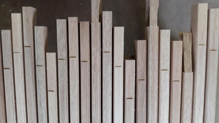 Eine Anordnung von Holzleisten in verschiedenen Längen. Die Leisten sind aus hellen Holzsorten und weisen saubere Schnitte auf.