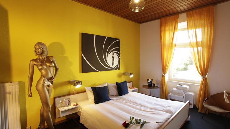 Une chambre moderne avec des murs jaunes et un grand lit double. Une statue dorée et une œuvre d'art donnent à la pièce un charme particulier.