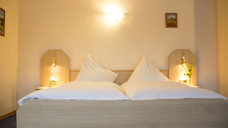 Ein gemütliches Schlafzimmer mit einem Doppelbett und zwei Kissen. Die Wände sind in neutralen Farben gehalten, und es gibt sanftes Licht von den Nachttischlampen.