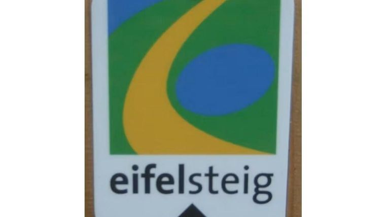 Ein Wegweiser für den Eifelsteig mit einer bunten Grafik. Der Pfeil zeigt nach oben und signalisiert den Wanderweg.