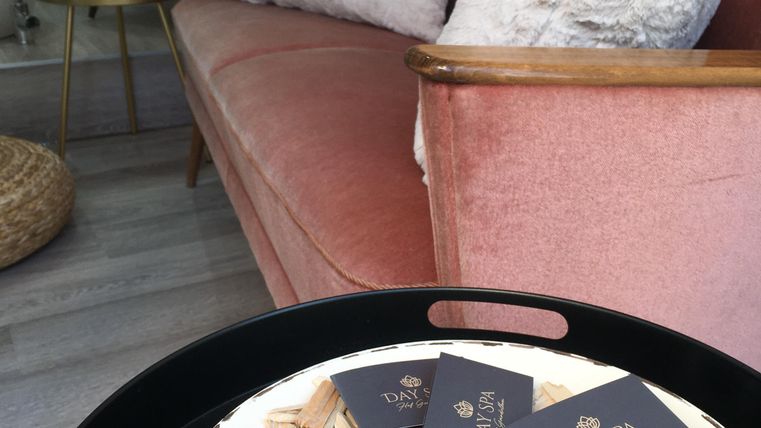 Une pièce élégante et confortable avec un canapé rose et des coussins décoratifs. Sur une table, il y a des bons spa et une petite décoration en couronne de fleurs.