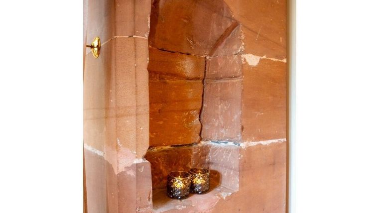 Eine Nische in einer Wand aus rotem Stein, in der zwei dekorative Kerzenhalter stehen. Die Nische hat eine natürliche, rustikale Gestaltung.