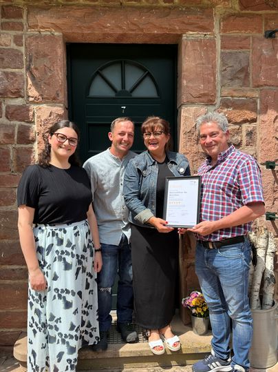 Vier erfreute und lachende Personen stehen vor einer Eingangstür und halten Stolz die Urkunde für die Klassifizierung in den Händen.