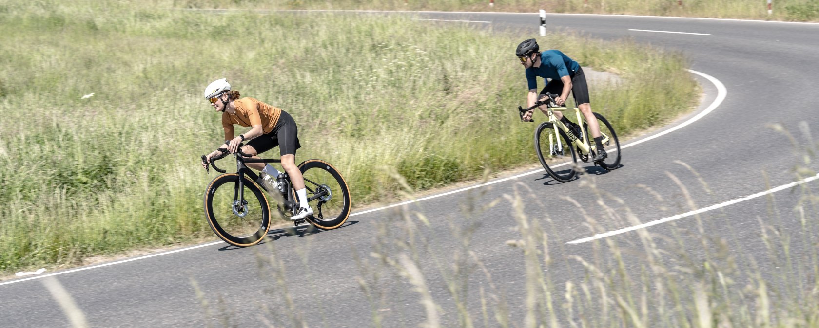 Twee fietsers rijden over een kronkelende landweg door een groen landschap in de Eifel. Ze dragen helmen en sportieve kleding., &copy; Eifel Tourismus GmbH, DennisStratmann