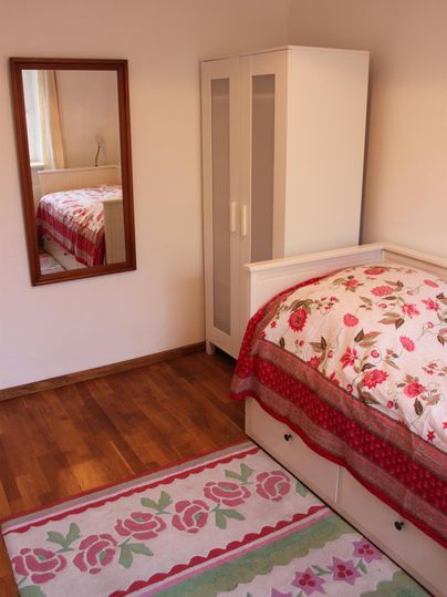 Een gezellige slaapkamer met een eenpersoonsbed, een kast en een spiegel. De vloer is versierd met een kleurrijk tapijt.