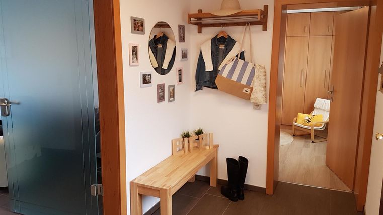 Ein einladender Flur mit einem Holzbank, Bildern an der Wand und einer Umkleidegarderobe. Auf der rechten Seite ist ein weiterer Raum mit einem hellen Sessel sichtbar.