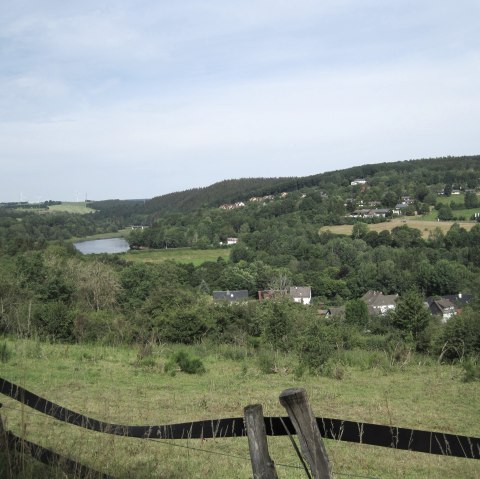 Groen landschap met uitzicht op het Kronenburger Meer, omringd door heuvels en windturbines op de achtergrond., &copy; Touristik GmbH Gerolsteiner Land