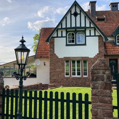 Une maison charmante avec un toit en tuiles rouges et un jardin vert. Devant la maison se trouve une lanterne et une clôture en bois.