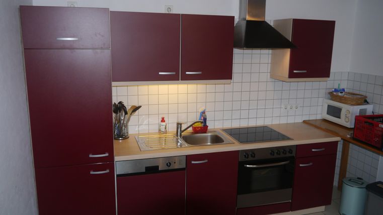 Eine moderne Küche mit roten Schränken und einer hellen Arbeitsplatte. Sie verfügt über einen Herd, eine Spüle und einige Küchengeräte.