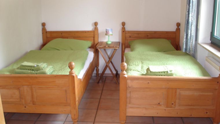 Een eenvoudige kamer met twee houten eenpersoonsbedden. De bedden zijn voorzien van groene bedlakens en handdoeken.
