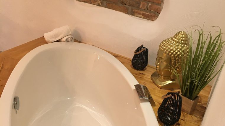 Une salle de bains élégante avec une baignoire blanche et une table en bois. Des éléments décoratifs comme des plantes et des bougies créent une atmosphère relaxante.