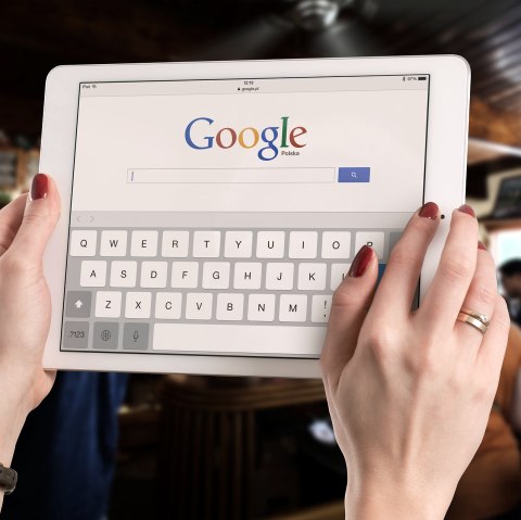 Nahaufnahme zweier Hände, die ein Tablet halten, auf dem Google geöffnet ist.