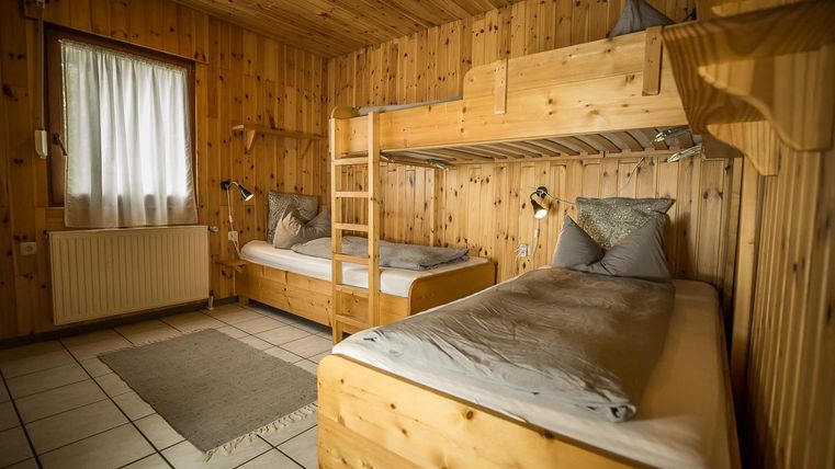 Een gezellige slaapkamer met houten bekleding. Er is een stapelbed en een eenpersoonsbed, beide met eenvoudige beddengoed.