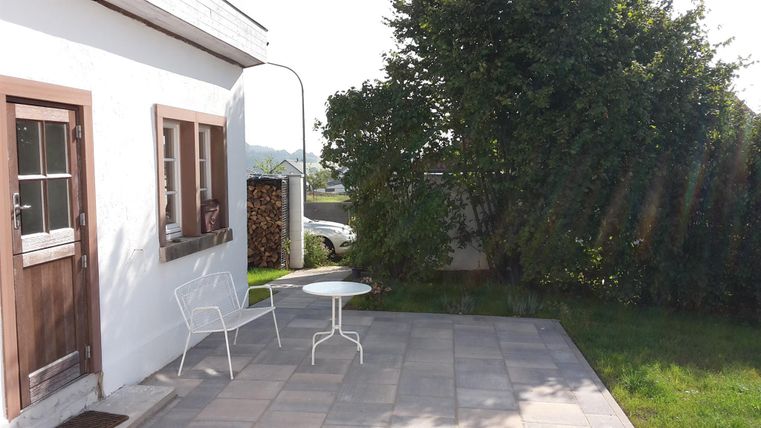 Een gezellige buitenruimte met een witte tafel- en stoelcombinatie. Op de achtergrond is een groene boom en een rustige omgeving te zien.