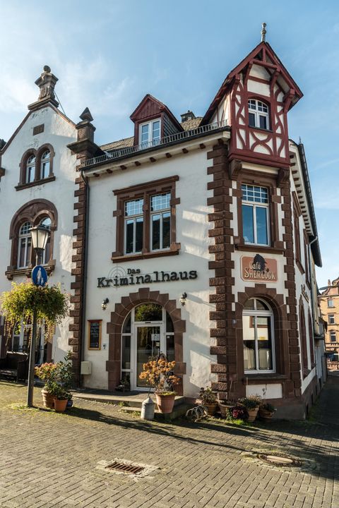Historisches Gebäude mit Fachwerkdetails, beschriftet als 'Das Kriminalhaus' und 'Café Sherlock', bei sonnigem Wetter in Hillesheim.