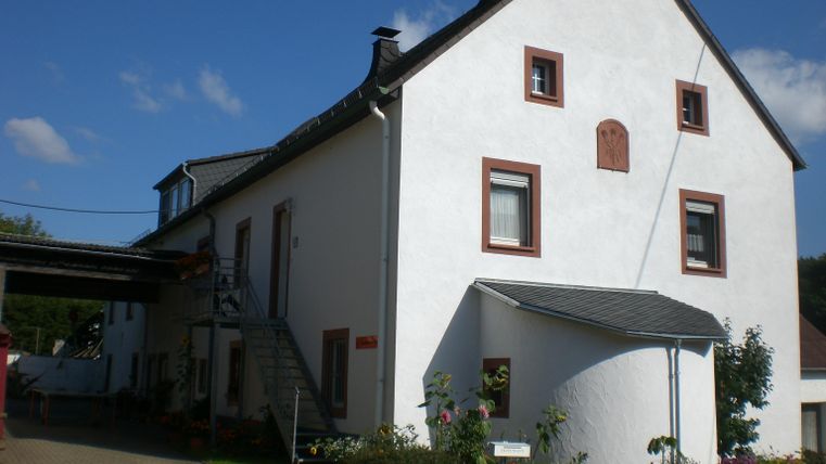Ein weißes Haus mit einem grauen Dach und runder Eingangstür. Im Vordergrund befindet sich ein kleiner Garten.