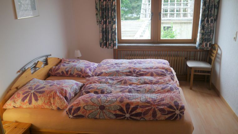 Ein gemütliches Schlafzimmer mit einem Doppelbett und bunten Bettdecken. Durch das große Fenster sieht man einen Blick ins Freie.