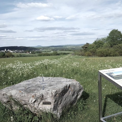 Green meadow with rocks and information board, in the background a village and hills under a blue sky., © Touristik GmbH Gerolsteiner Land