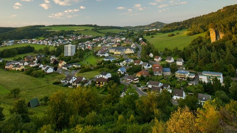 Vue panoramique de Gerolstein avec des maisons, des prairies et des collines boisées en arrière-plan.