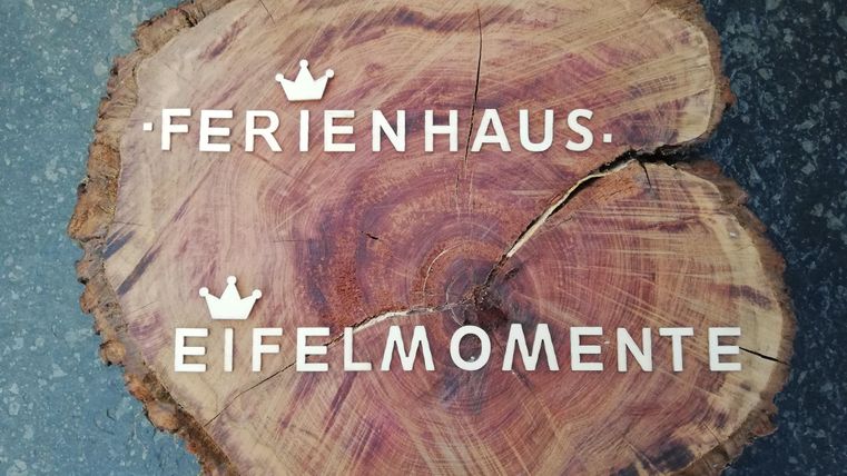 Een houten bord met de opschriften "Vakantiehuis" en "Eifelmomenten". Het is gemaakt van natuurlijk hout en heeft een rustieke uitstraling.