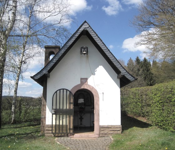 Small white chapel with a black roof, surrounded by trees and hedges, under a blue sky., © Touristik GmbH Gerolsteiner Land, Ute Klinkhammer