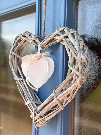 Ein dekoratives Herz aus Weidenruten hängt an einer blauen Tür. Es enthält ein weißes Herz in der Mitte.
