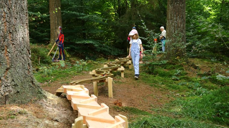 Kinder spielen an einer hölzernen Kugelbahn im Wald.