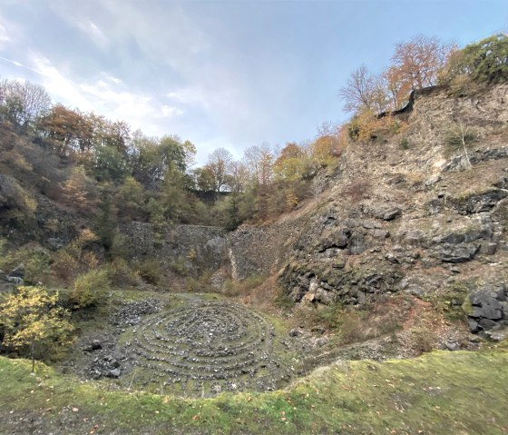 The interior of the massive volcanic quarry, surrounded by trees with colorful foliage under a blue sky., © Touristik GmbH Gerolsteiner Land