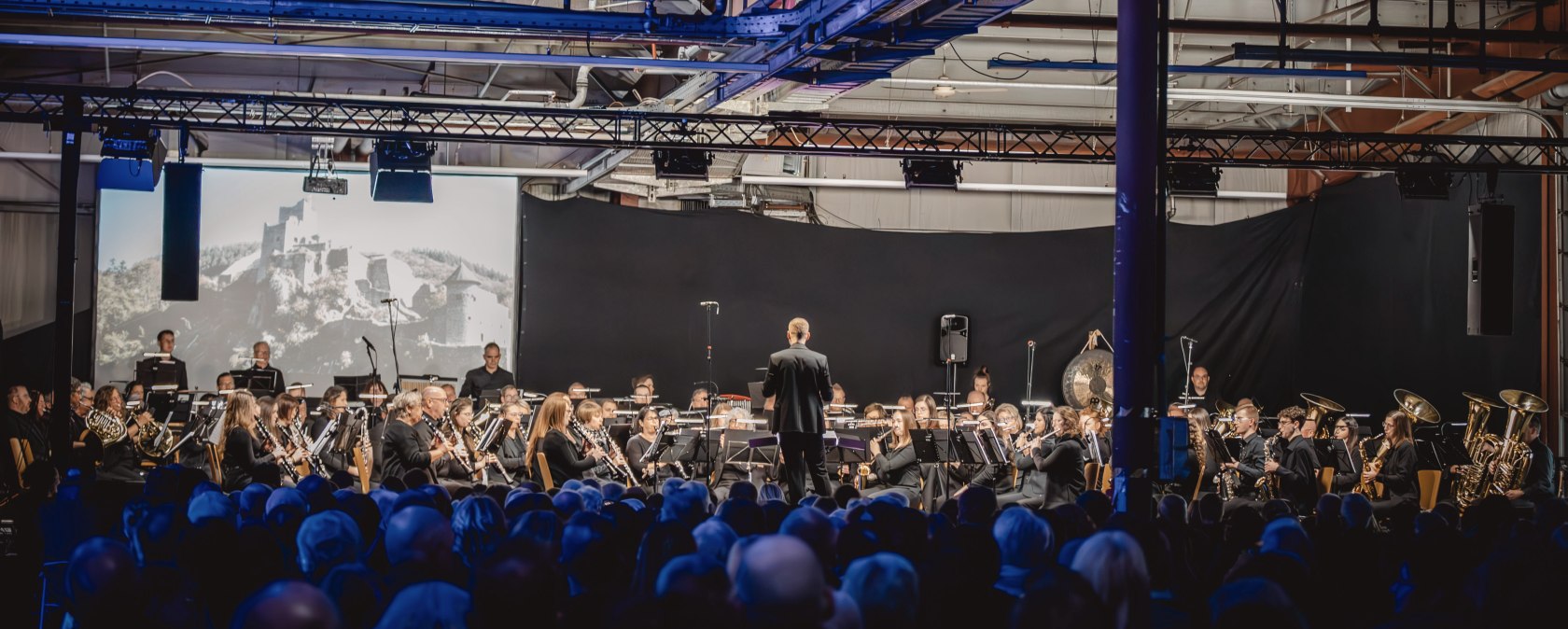Dunkle Halle, inder ein großes Orchester vor großem Publikum musiziert.