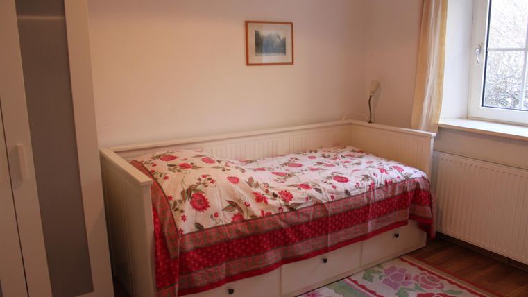 Een eenvoudige slaapkamer met een bed dat een bloeiende dekbed heeft. Naast het bed staat een kast, en een raam zorgt voor natuurlijk licht.