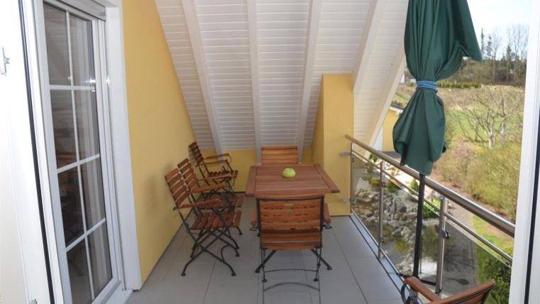 Een gezellige balkon met houten stoelen en een tafel. De wanden zijn geel geverfd en er is een mooi uitzicht op het groen.