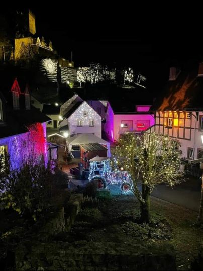 Eine malerische Nachtansicht eines kleinen Dorfes, beleuchtet von bunten Lichtern. Im Hintergrund sieht man eine Burg, die ebenfalls erleuchtet ist.