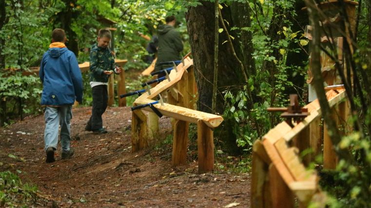 Kinder spielen im Wald neben eienr Waldkugelbahn mit ihrem Kugeln.