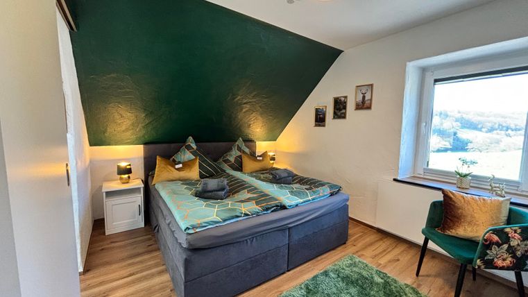 Ein modernes Schlafzimmer mit einem Doppelbett und grünen Akzenten. Das Zimmer hat ein Fenster mit Blick nach draußen und eine gemütliche Sitzecke.