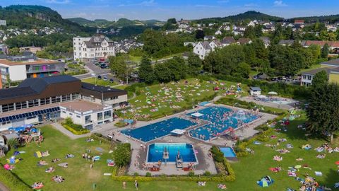Luftaufnahme des Freibads Gerolstein mit mehreren Schwimmbecken und vielen Menschen auf der Liegewiese. Im Hintergrund sind Gebäude und Hügel.