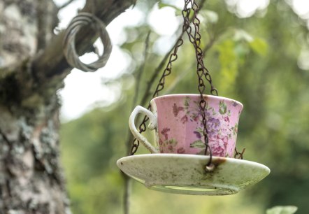 Eine rosa Tasse mit Blumenmuster h&auml;ngt an einer Kette an einem Ast in einem gr&uuml;nen, bewaldeten Umfeld., &copy; Eifel Tourismus GmbH, Dominik Ketz